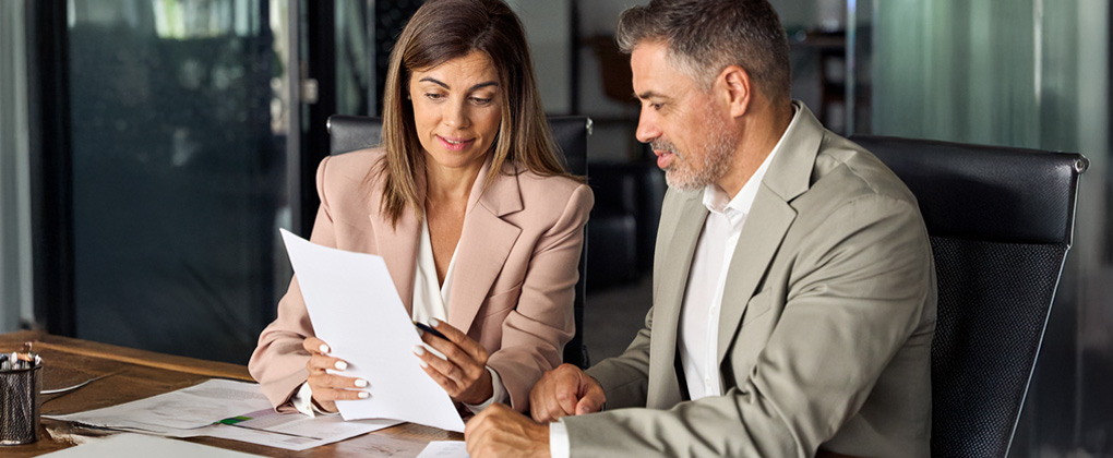Un homme et une femme parlent dans un bureau, elle tient une feuille blanche à la main.