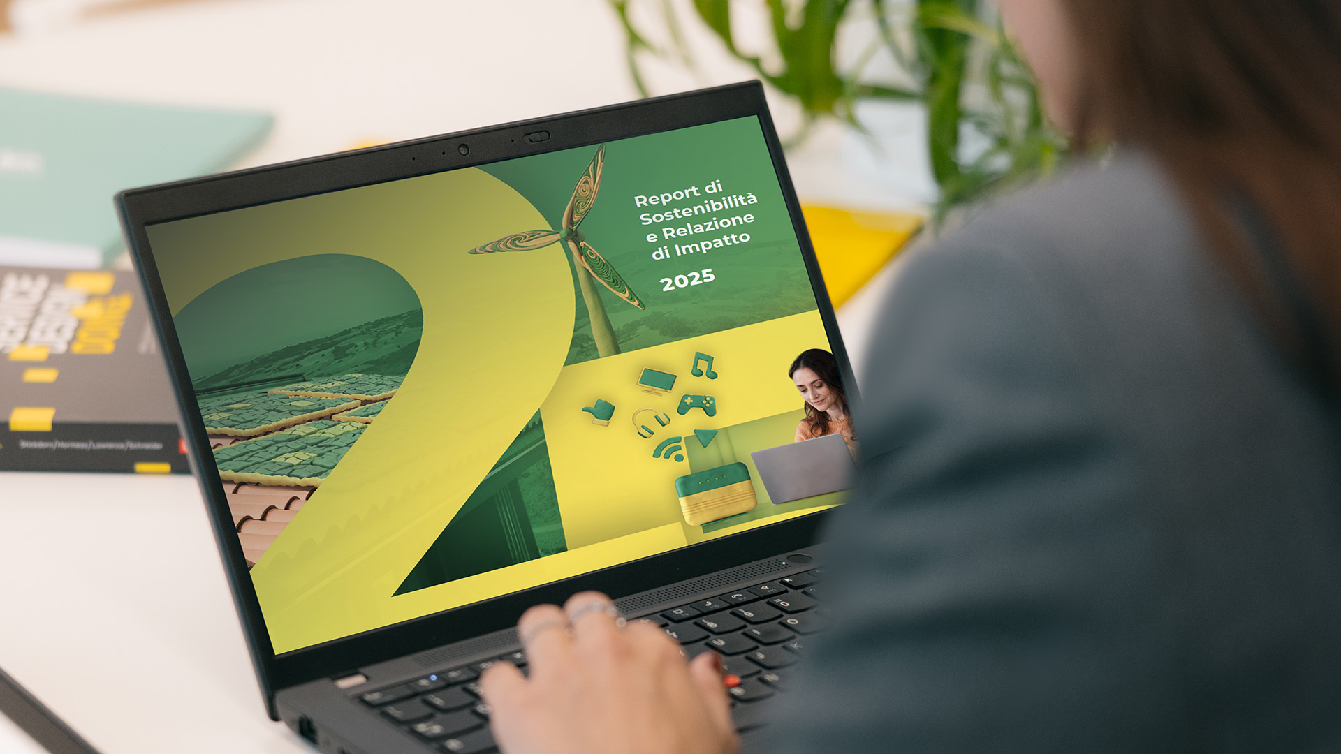 Una donna di spalle guarda un pc, sullo schermo c’è la copertina del Report di Sostenibilità e Relazione di Impatto di Plenitude.