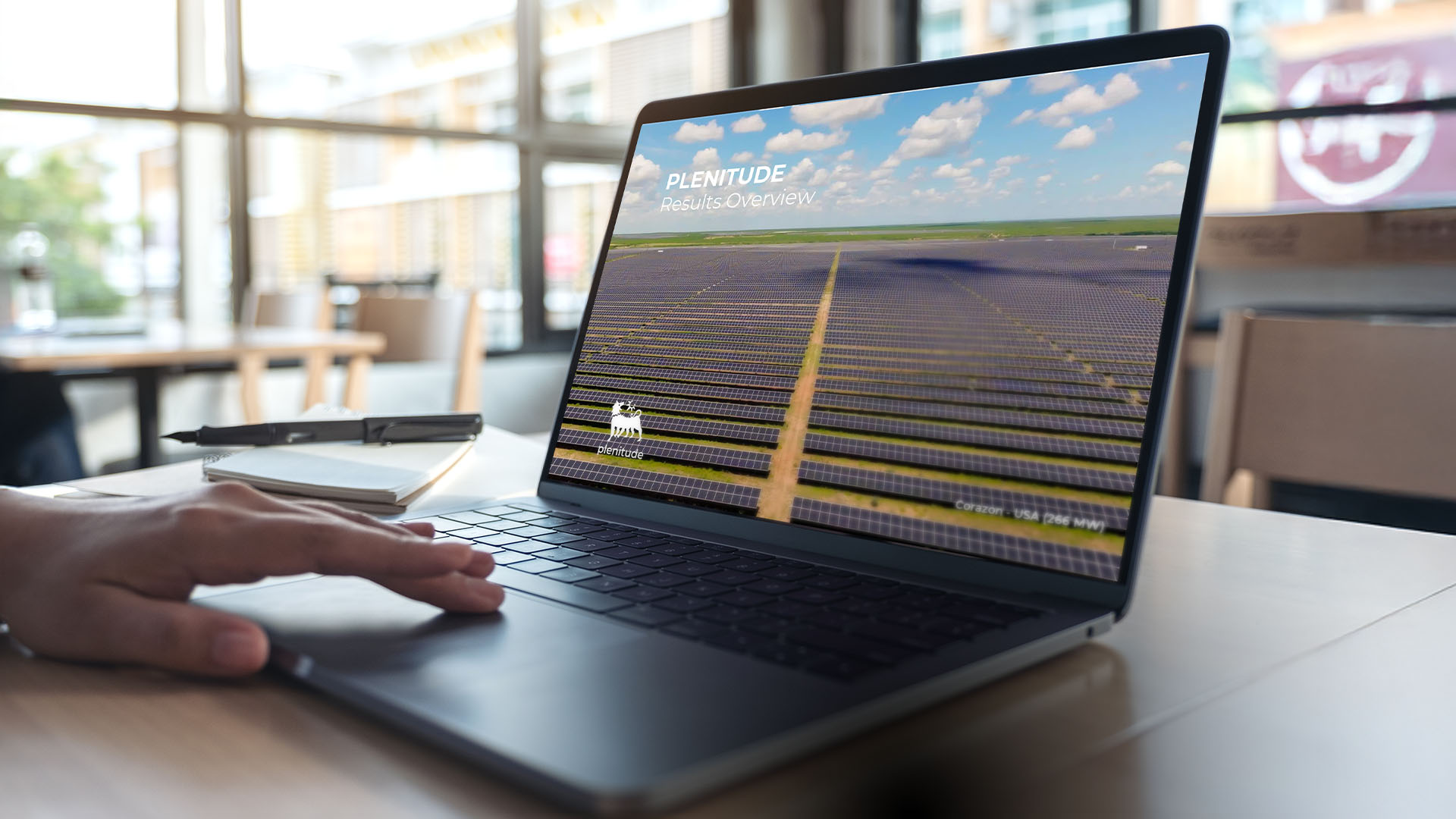 Un laptop aperto appoggiato su un tavolo, sullo schermo la scritta “Plenitude Results Overview”, il logo di Eni Plenitude e sullo sfondo un parco fotovoltaico.